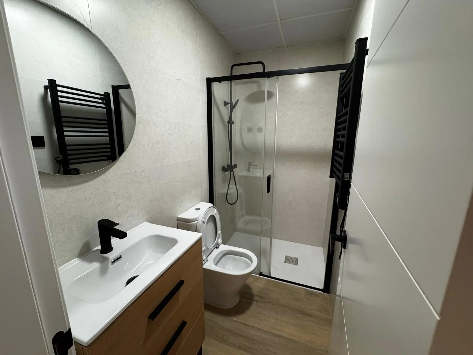 Baño terminado con ducha, grifería negra y mueble de madera
